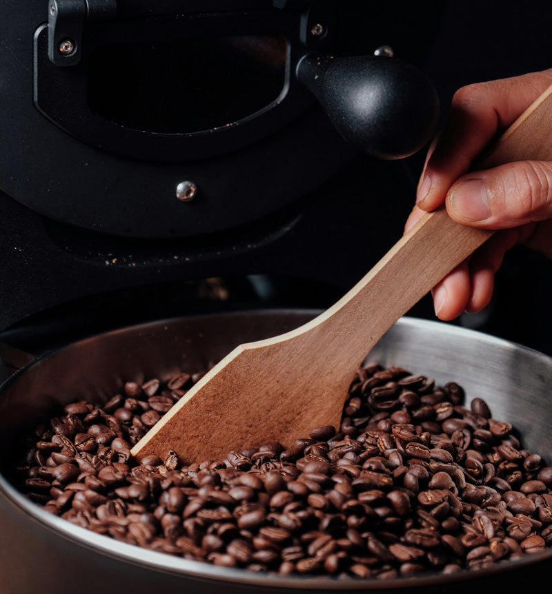 Person stirring flavored roasted coffee beans in a pan with a wooden spatula in sumner, iowa